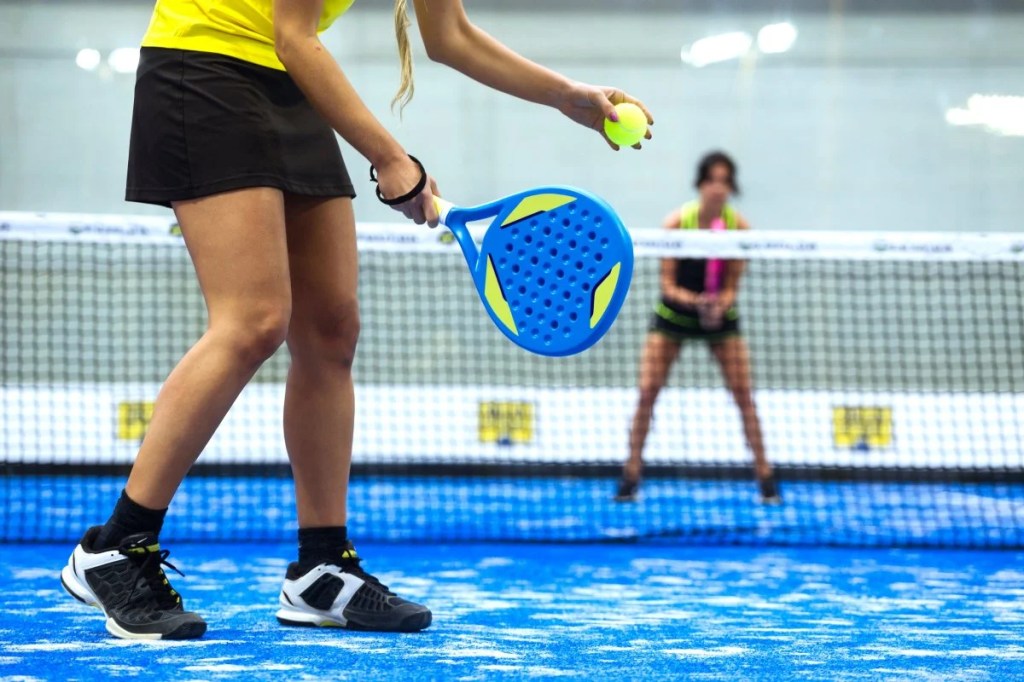 Two people playing paddle tennis on a blue court with green balls 